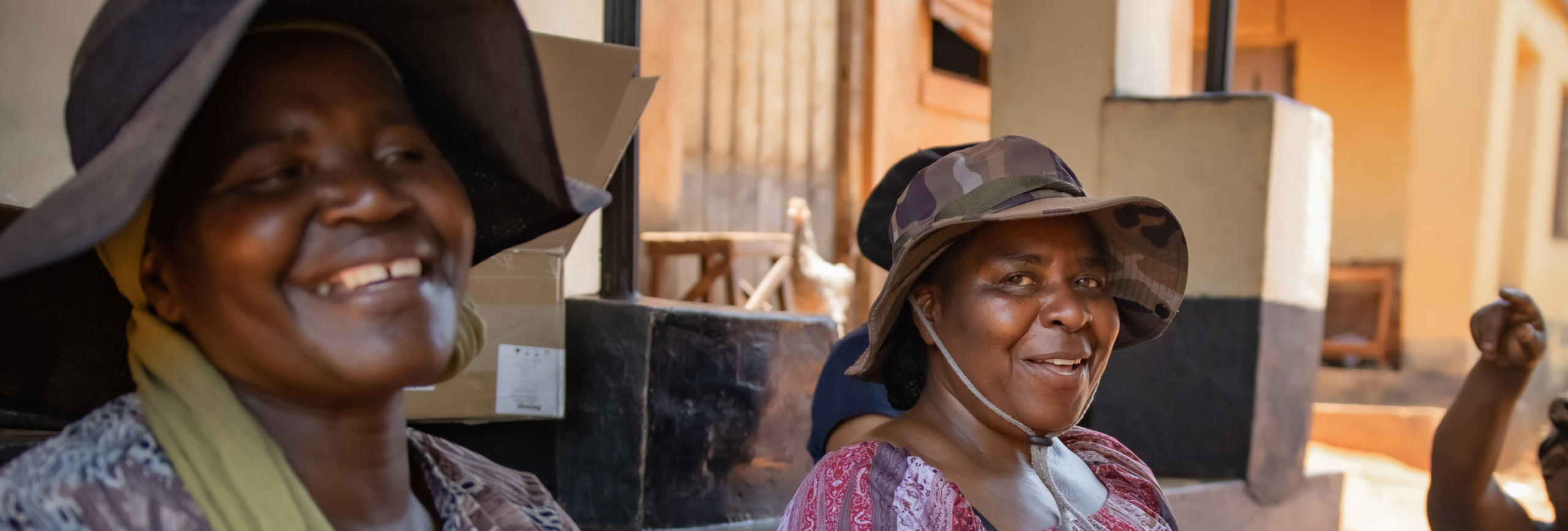 Two women smile, wearing hats looking at the camera.