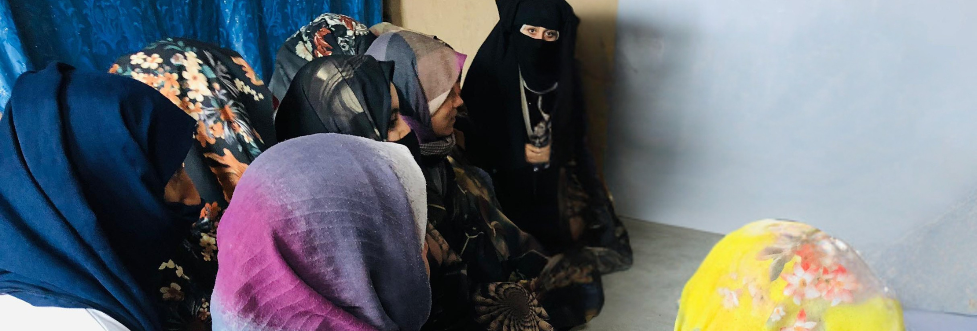 A group of Afghan women gather in conversation, sat on the floor.