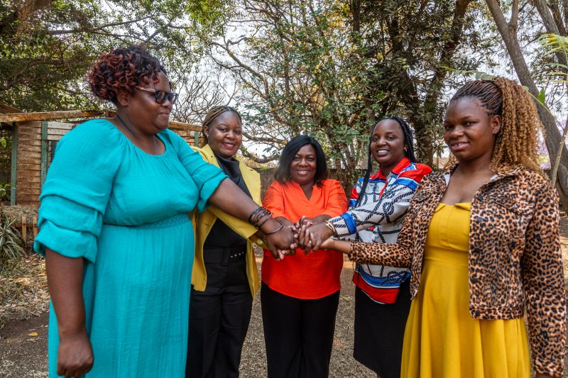 Five members of the Women and Land Zimbabwe team gather with their hands placed together in the middle of a circle.